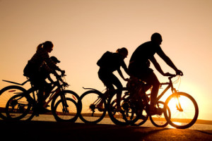 Image of sporty company  friends on bicycles outdoors against sunset. Silhouette